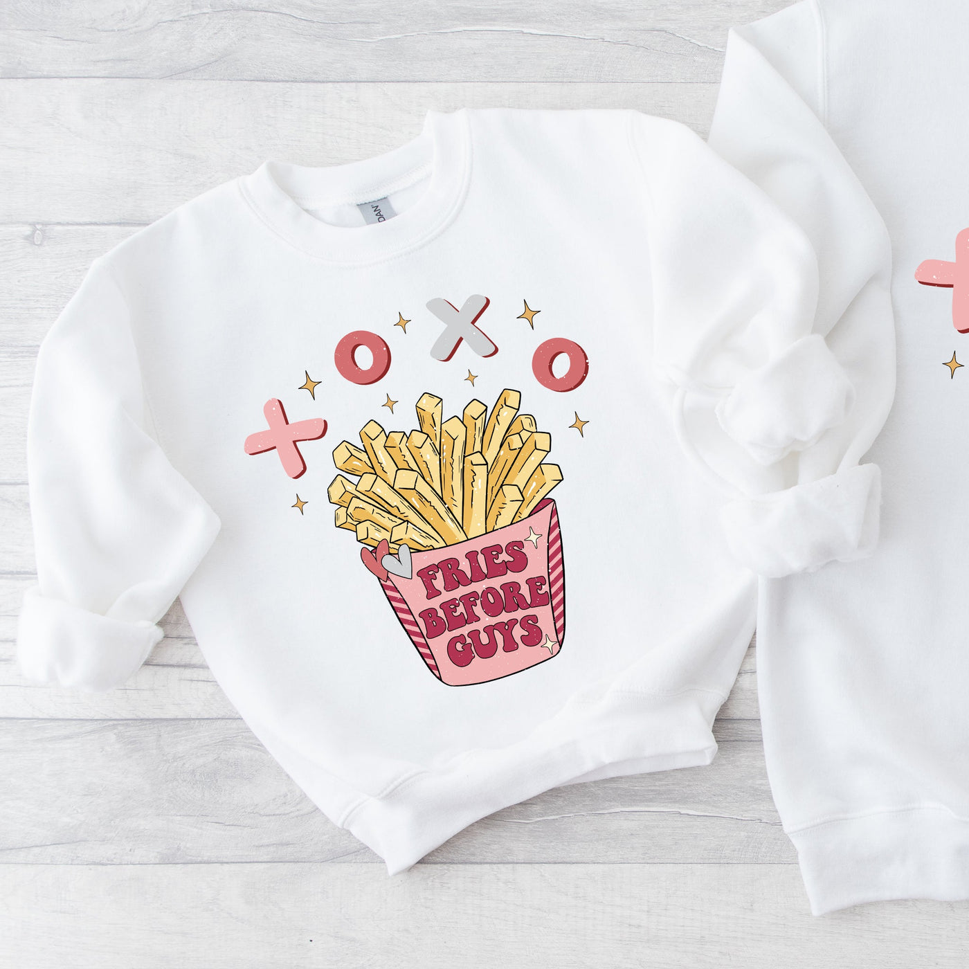 Two white sweatshirts with French fry design and text on a light wooden surface