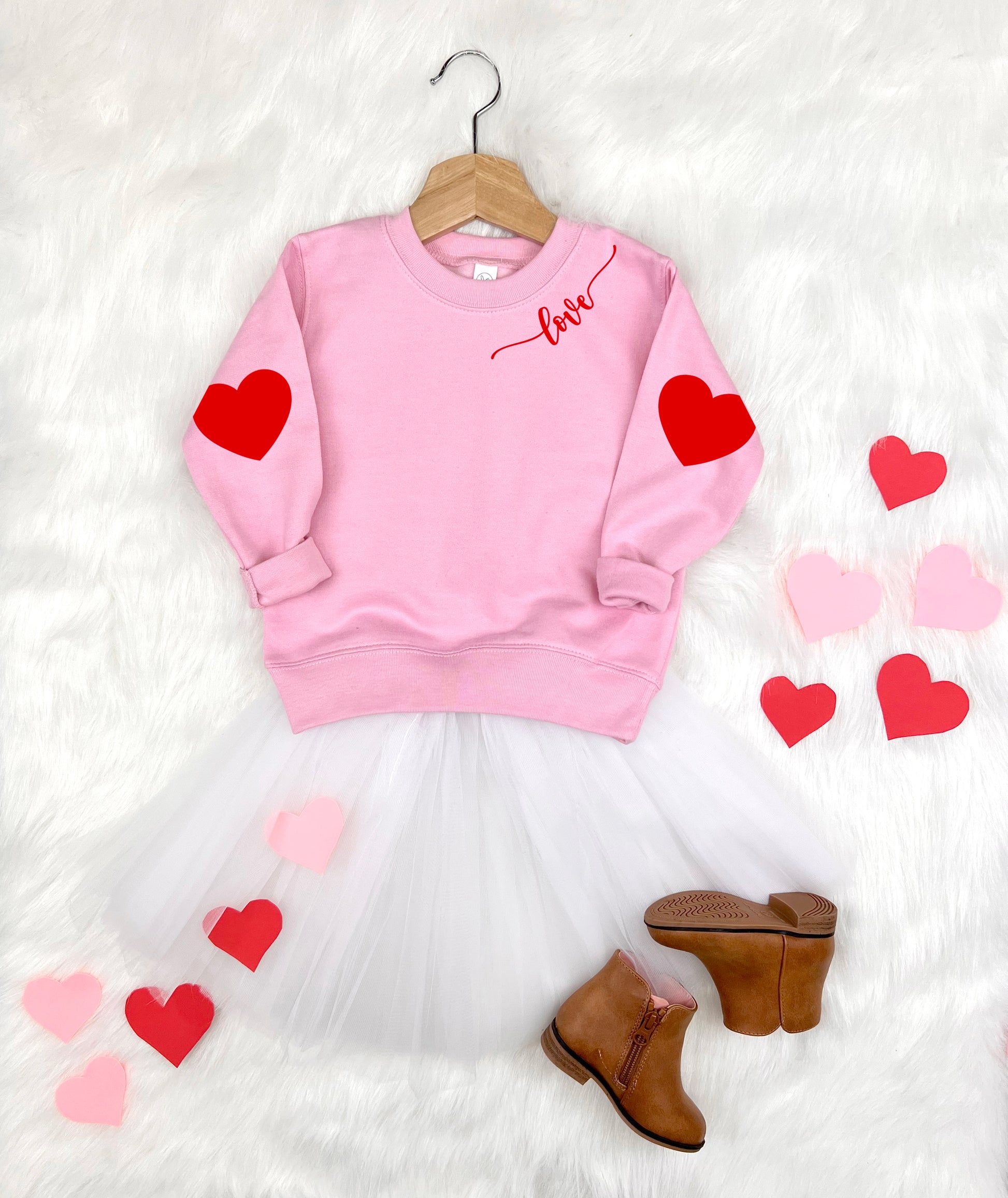 Pink sweatshirt with red hearts and 'love' text, white tutu, brown boots on a white background.