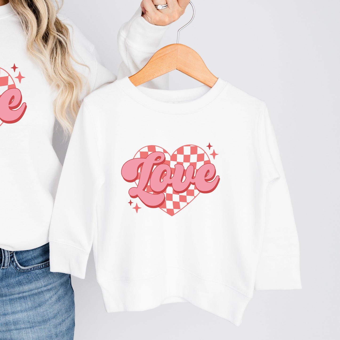 White sweatshirt with pink 'Love' design held by a person against a plain background