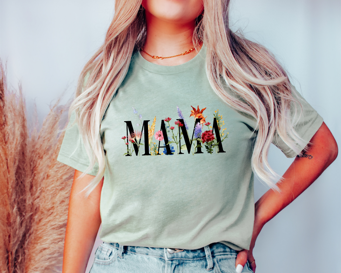 Person wearing a light green t-shirt with 'MAMA' and floral designs, standing against a plain background.